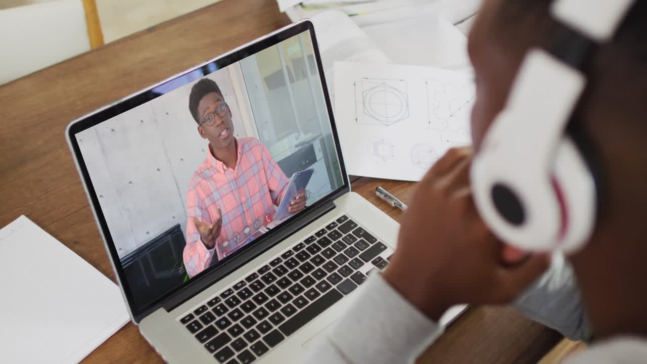 estudiante universitario afroamericano que sostiene notas mientras hace una videollamada en una computadora portátil en casa