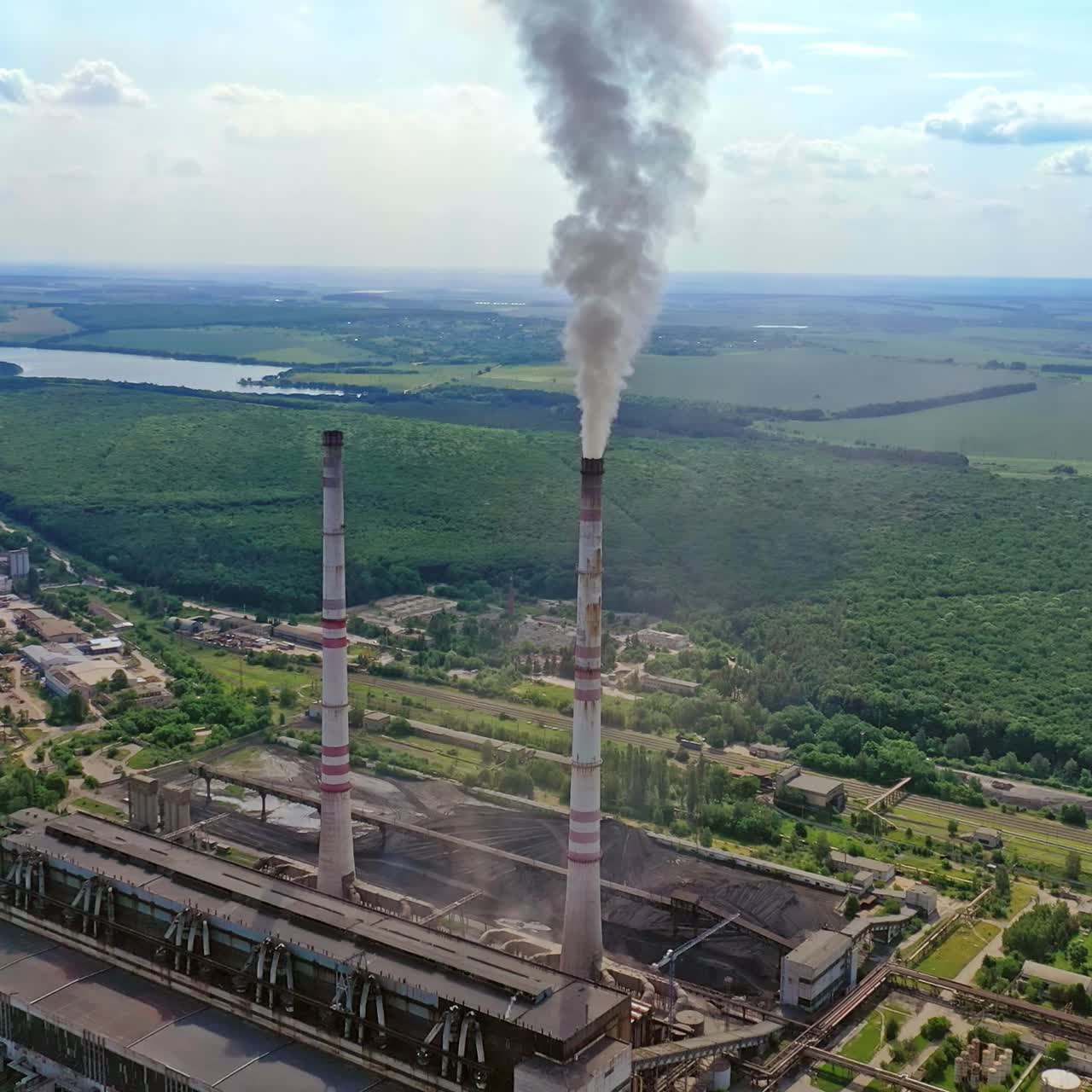 Industrial area in nature. Industrial pipes with smoke. Metallurgical factory with pipes among green field. Aerial view.
