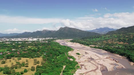 drone hyperlapse zoom in towards yopal, colombia, revealing urban areas, riverbed and lush green mountains under a bright sky