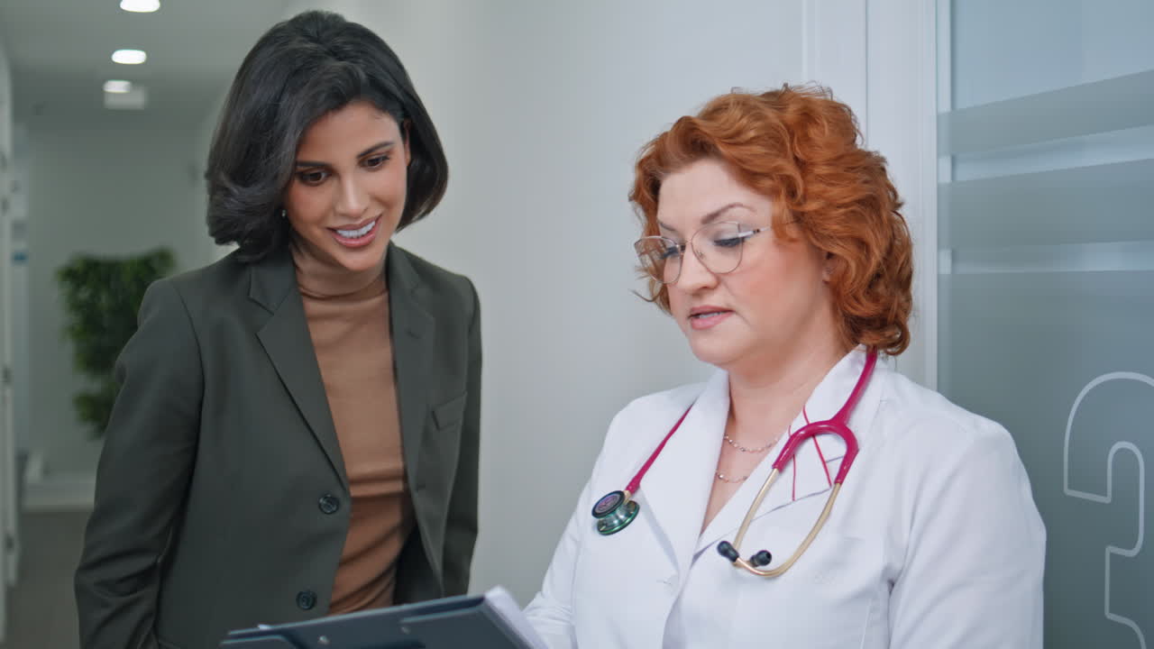 Healthcare specialist showing clipboard to woman patient in medical hall closeup