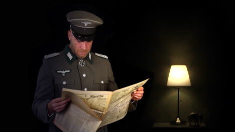 german world war two wehrmacht army officer in grey uniform reading a newspaper in a dark room with a lamp