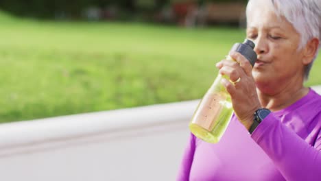 Video-of-tired-biracial-senior-couple-drinking-water-after-tennis-training