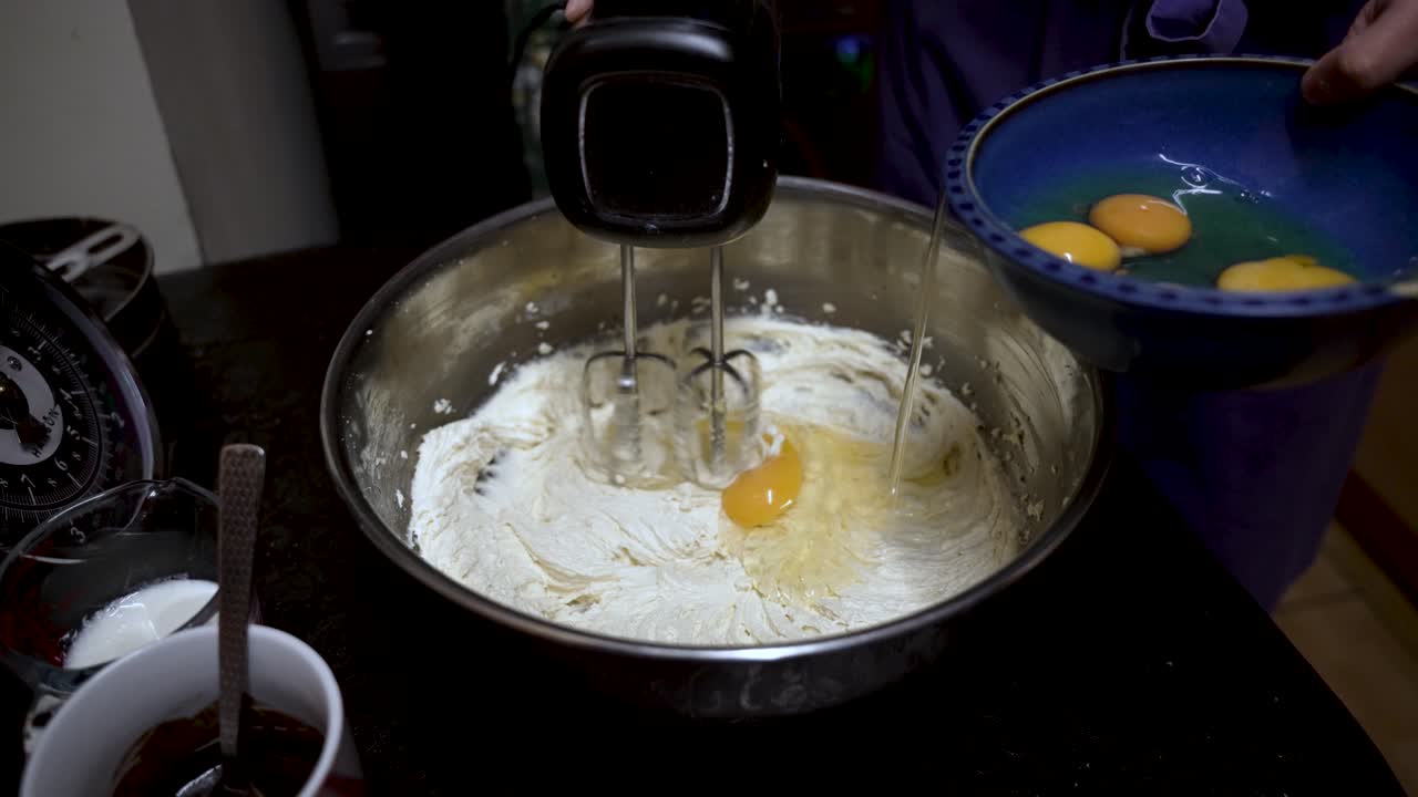 Mixing batter in a bowl with an electric mixer while adding egg yolks. slow motion