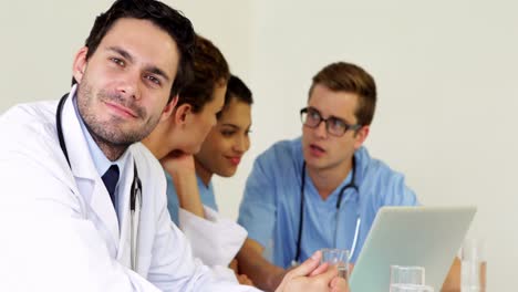 Doctor-smiling-at-camera-while-colleagues-are-talking