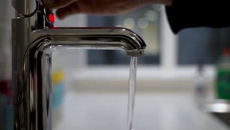 agua caliente que fluye del grifo del fregadero de la cocina moderna con indicador de luz roja de primer plano