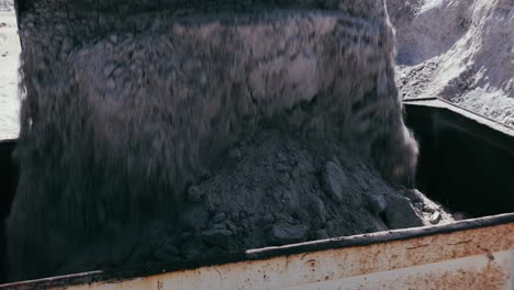 aerial view of an excavator dumping raw material into a dump truck at an open-pit mining site