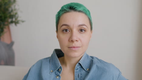 vista de cerca de una mujer con cabello azul con los ojos cerrados, abre los ojos y mira a la cámara