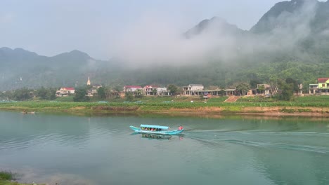 a tourist boat moving in a beautiful river with the reflection of the misty mountain at background