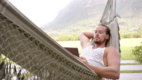 a young caucasian man with long brown hair and beard relaxes in a hammock