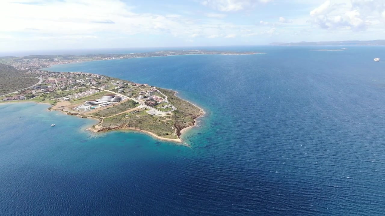 Vista aerea con drone che mostra la Penisola di Gallipoli che si estende nelle acque blu intenso del Mediterraneo, con bassi fondali turchesi, strade costiere, edifici e terreno verde visibili