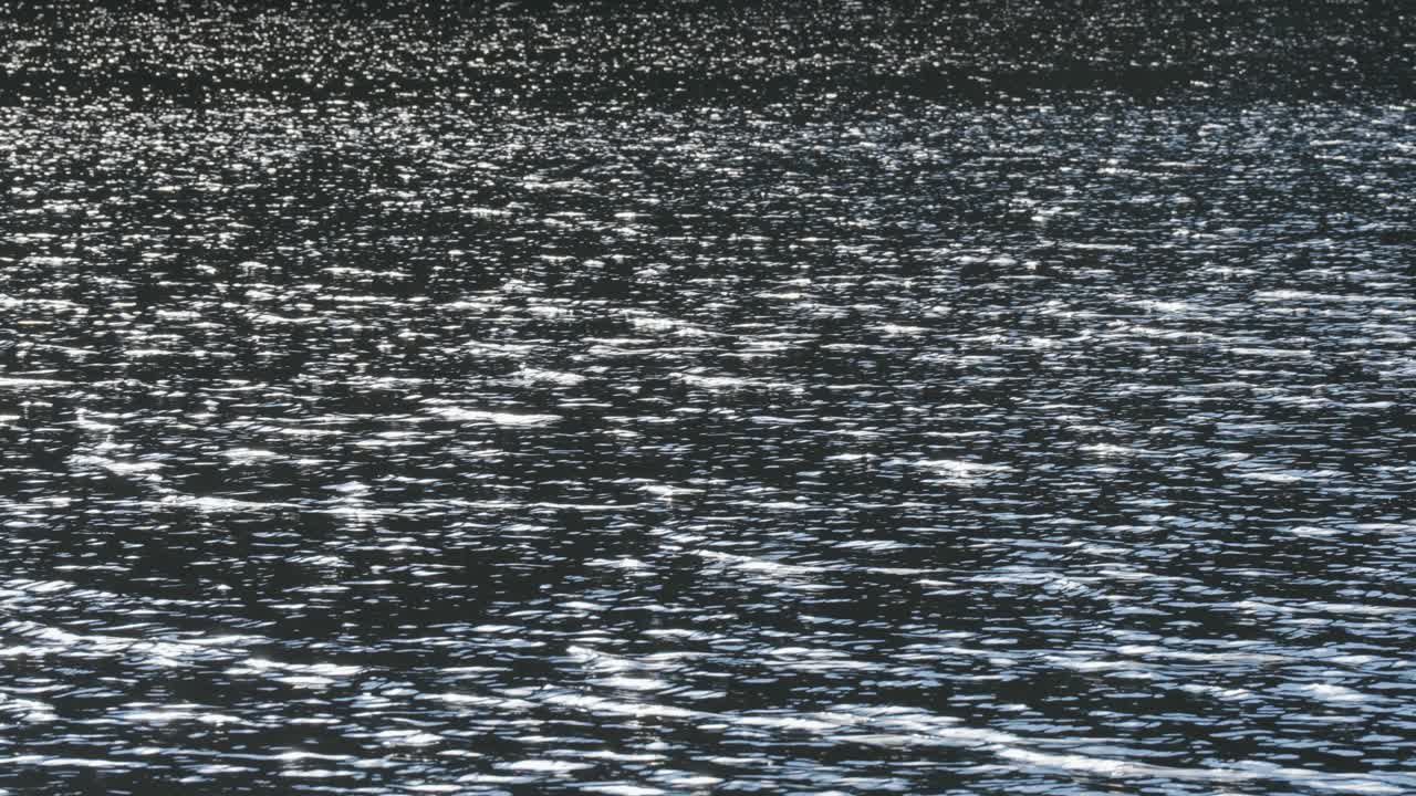 Shimmering light reflections dance on a water surface, creating a dynamic and sparkling effect.