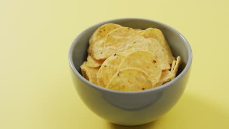 Close-up-of-chips-in-a-bowl-with-copy-space-on-yellow-surface