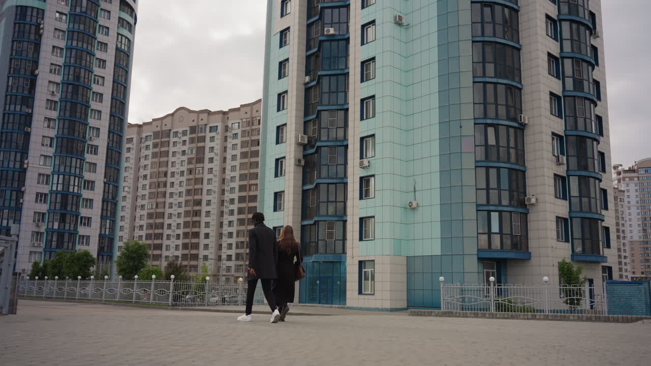 Leg view shows two students walking on paved promenade between tall city buildings, black and white sneakers contrast against modern architecture, creating balanced motion and urban street t