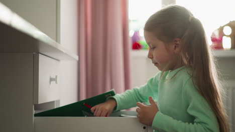 Happy-girl-finds-markers-pack-under-folder-in-desk-drawer