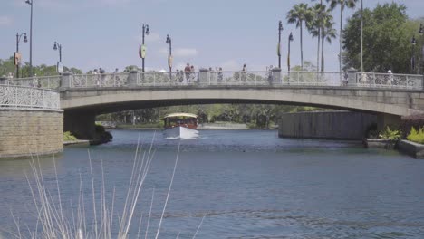 A-slow-moving-passenger-boat-travels-underneath-a-busy-bridge-full-of-people