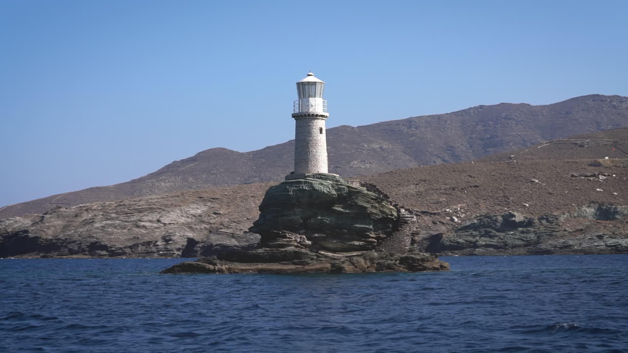 un faro solitario en un islote rocoso en el océano azul claro, con afloramientos rocosos cercanos visibles bajo un cielo nublado