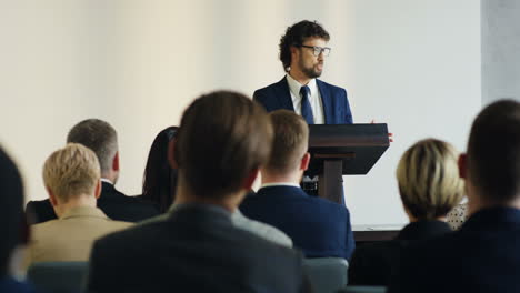 caucasian businessman standing in front of a big audience while people rising hands for asking questions at a business conference