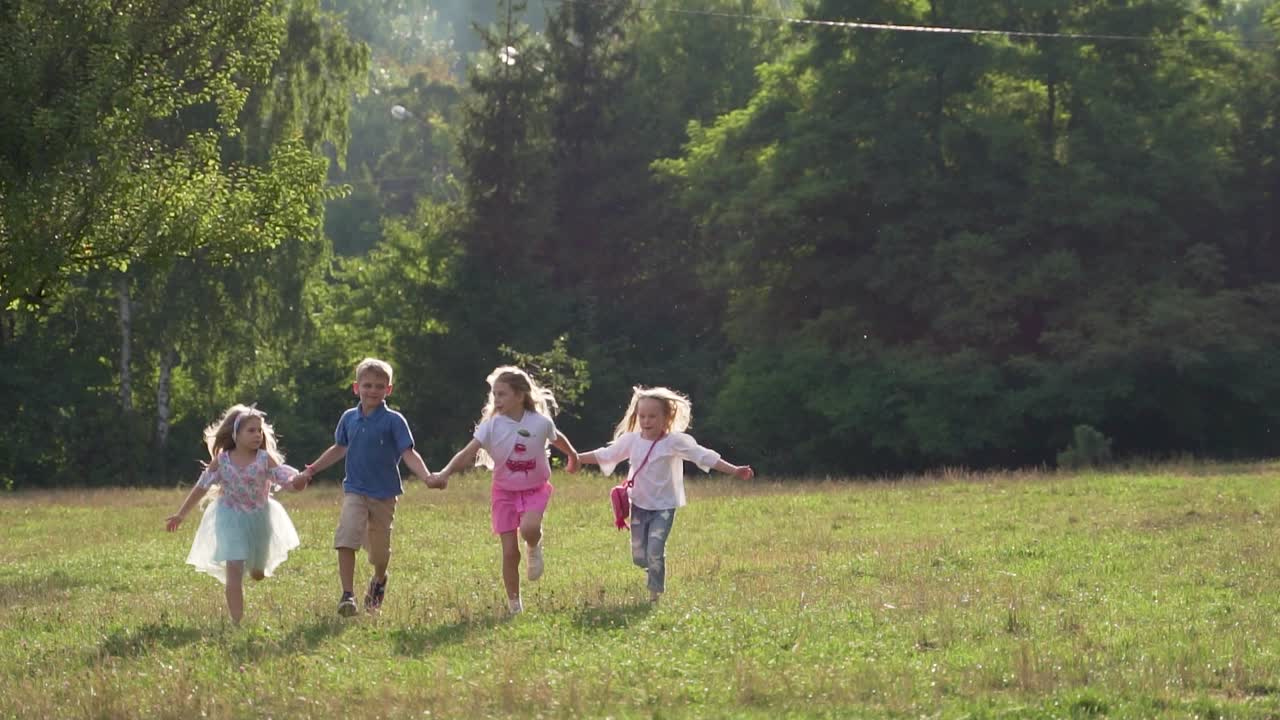 Cheerful children run along the green grass in the park holding hands. Children's holiday, outdoor recreation. Slow motion