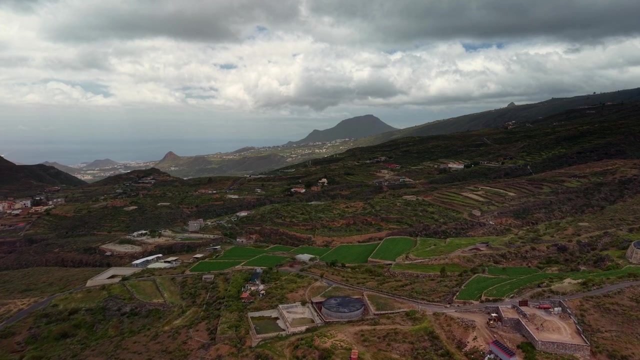 Vista aerea di colline vulcaniche terrazzate e campi rurali sotto cieli nuvolosi e drammatici.