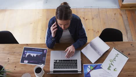 overhead view of woman talking on smartphone while using laptop