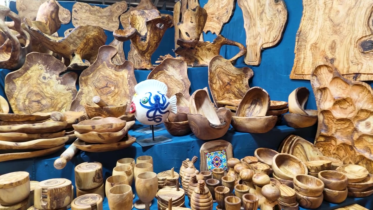 Un plano medio recorre un puesto de mercado lleno de utensilios de cocina artesanales de madera de olivo.