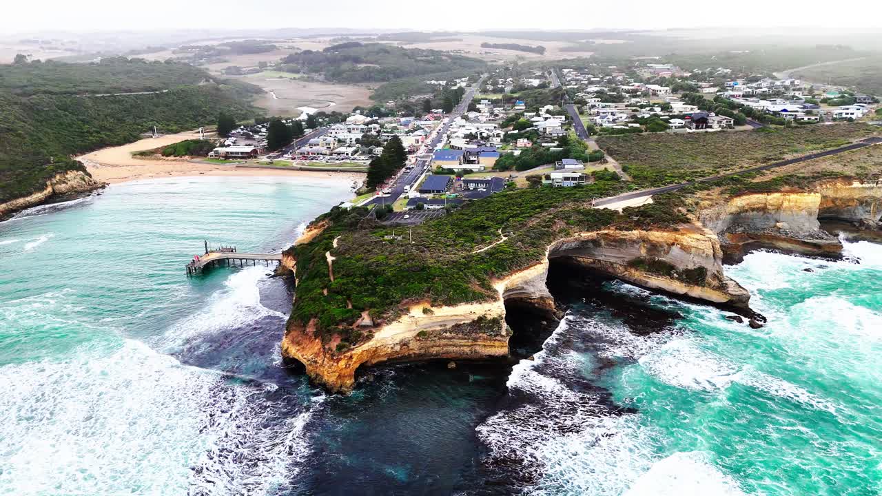 Drone footage captures Port Campbell's dramatic cliffs and turquoise waves under bright daylight, showcasing natural beauty and coastal erosion