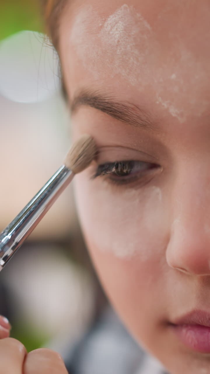 Makeupartist forbereder sig, ansigtstræk fremhævet af blid pudderpåføring backstage, professionel stylist forfiner folder og ansigtstræk med blød pudderglød og naturlig makeup.