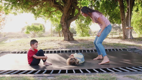 siblings with teenage sister playing on outdoor trampoline in garden