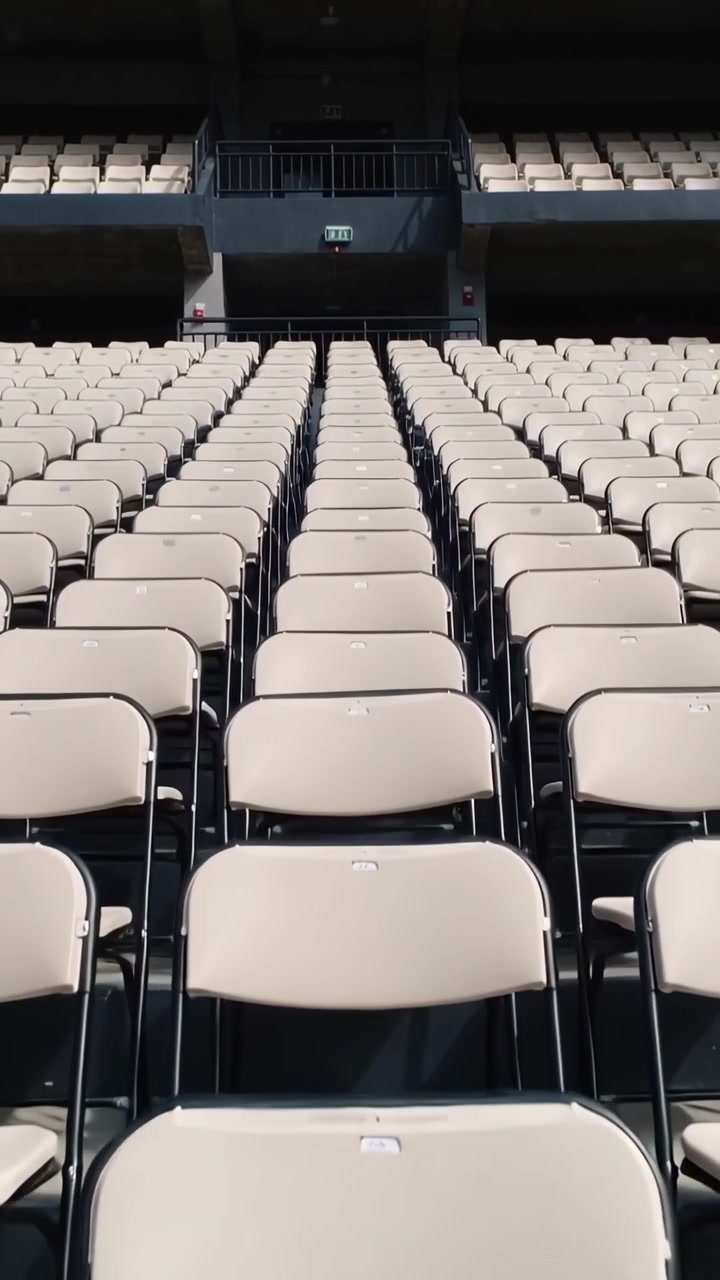 Video verticale: Telecamera che si inclina rivelando le sedie centrali per mostrare una ringhiera metallica e un'insegna di uscita in un'arena.