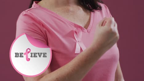 Animation-of-believe-text-over-caucasian-woman-with-pink-ribbon-on-pink-background