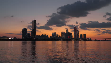 Silhouetted-Yeouido-Island-Bussines-District-and-63-Building-Skyscraper-in-Yeongdeungpo-gu-During-Colorful-Sunset-with-Dramaic-Sky,-View-form-Han-River-Park-Waterfront,-Iconic-Seoul-Skyline