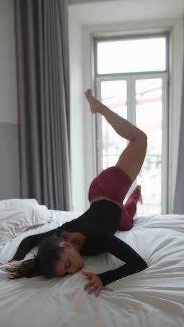 Woman practicing yoga on a bed near a window