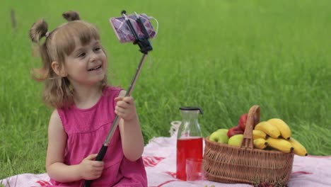 en un picnic de fin de semana. niña en el prado de hierba hace selfie en el teléfono móvil con un palo de selfie. llamada de video