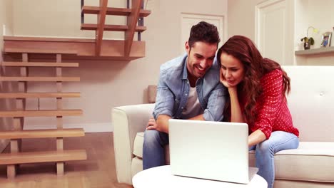 pareja feliz usando una computadora portátil en el sofá