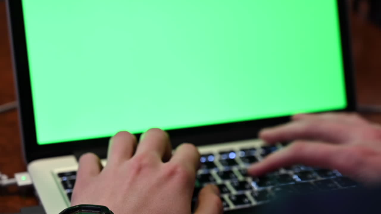 Close up of a man typing on a laptop with a green screen