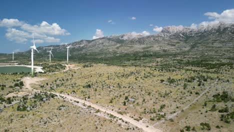 Drone-footage-over-arid-region,-velebit-mountain-range-with-wind-turbines-rotating-and-collected-water-in-two-lakes,-blue-and-green