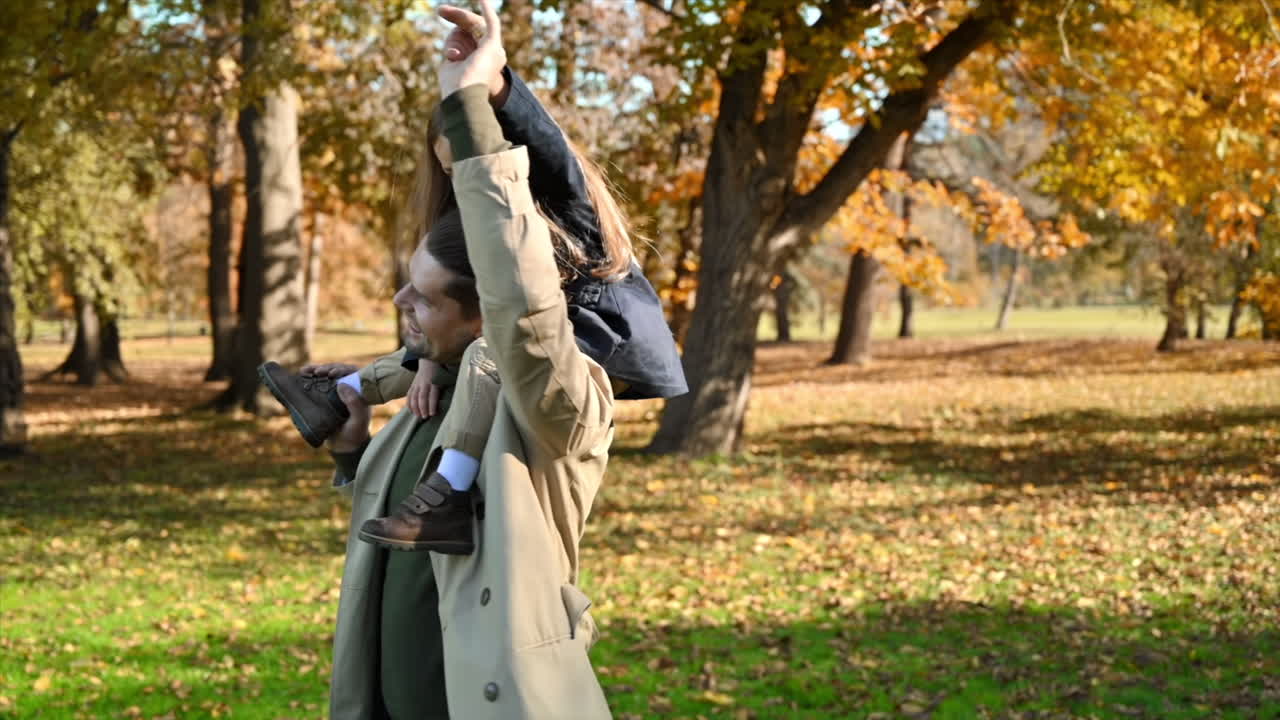 Happy family in an autumn park. Father put his daughter on his neck and plays, yellowed trees around. Slow motion