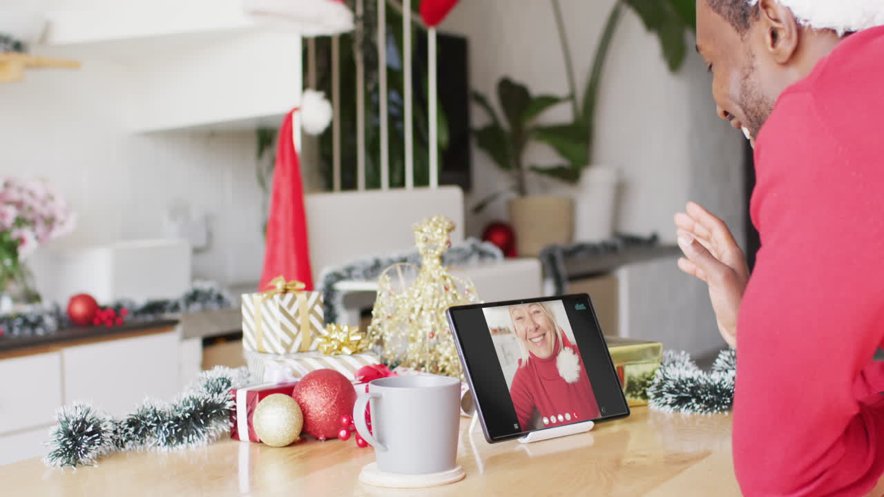 animación de un hombre afroamericano en sombrero de santa en una llamada de video de tableta con una mujer en navidad