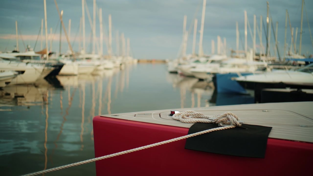 Primo piano di una cima d'ormeggio bianca avvolta sul ponte di uno yacht rosso e crema al porto turistico di Port Vauban ad Antibes, Francia, con barche a vela sfocate e riflessi sullo sfondo.