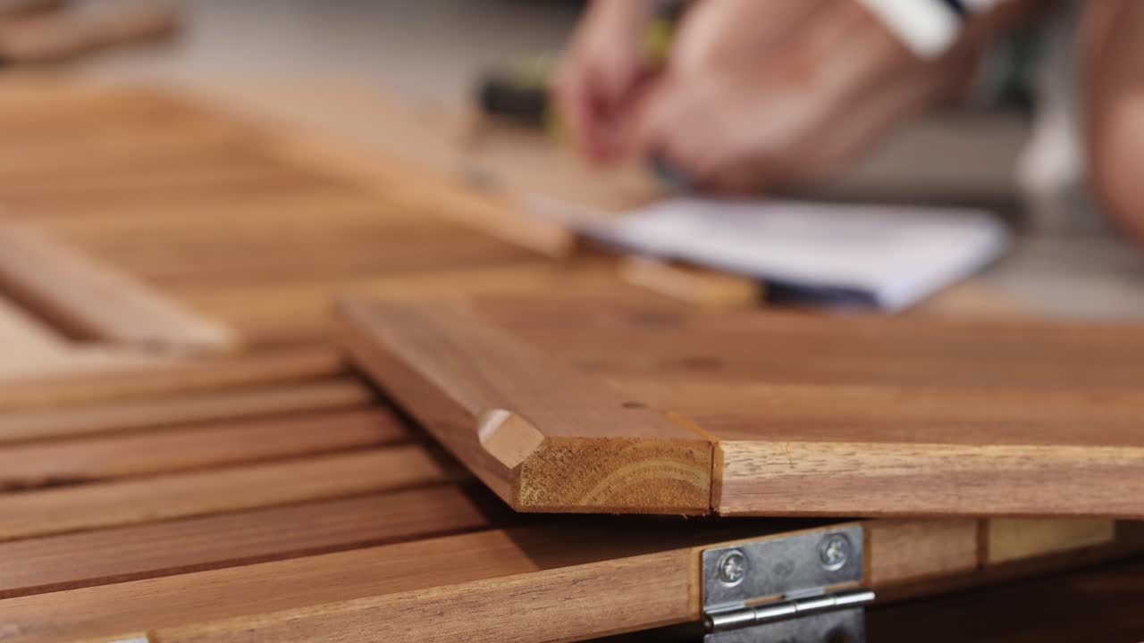 Hands assembling wooden furniture, focusing on detail and craftsmanship, with a blurred background for depth