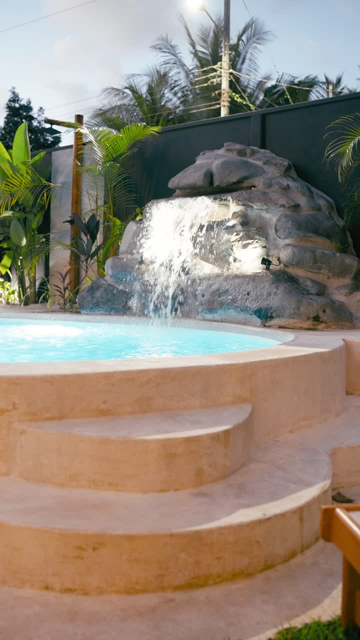 Udendørs swimmingpool med naturligt klippevandfald og tropiske planter