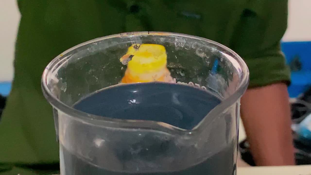 un recipiente de vidrio que contiene un líquido químico negro goteado con un líquido químico utilizando una pipeta