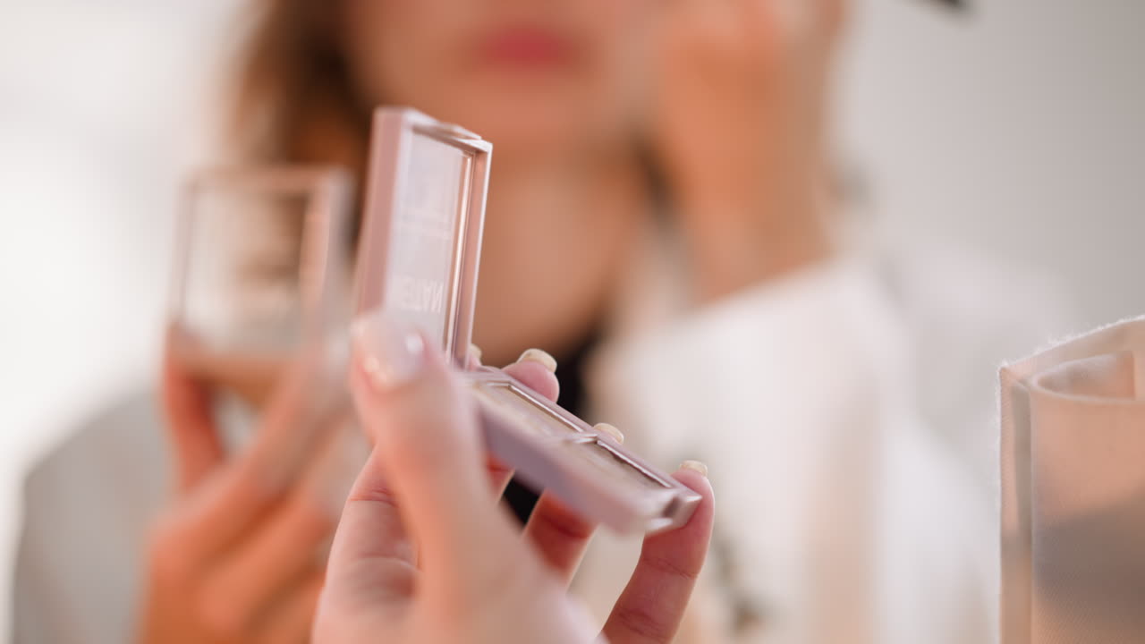 Mani di donna che reggono una palette di ombretti e un applicatore