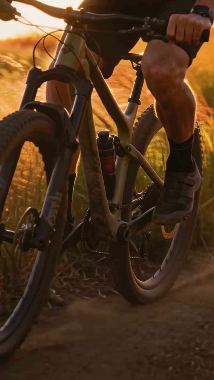 Video verticale: Ciclista in tenuta da bici vicino a una curva, che sterza su un sentiero sterrato, con pneumatici tassellati che sollevano polvere.
