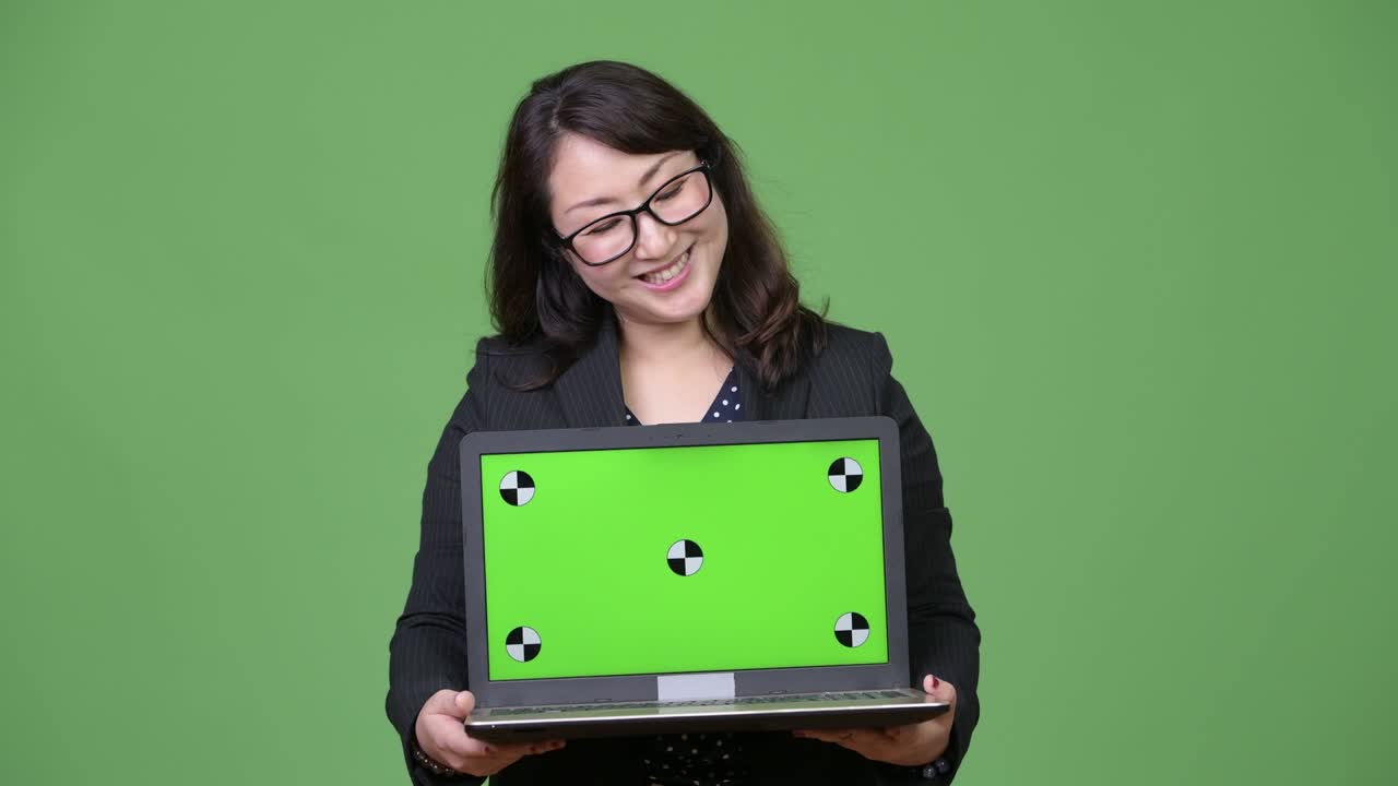 una hermosa mujer de negocios asiática madura mostrando una computadora portátil contra un fondo verde
