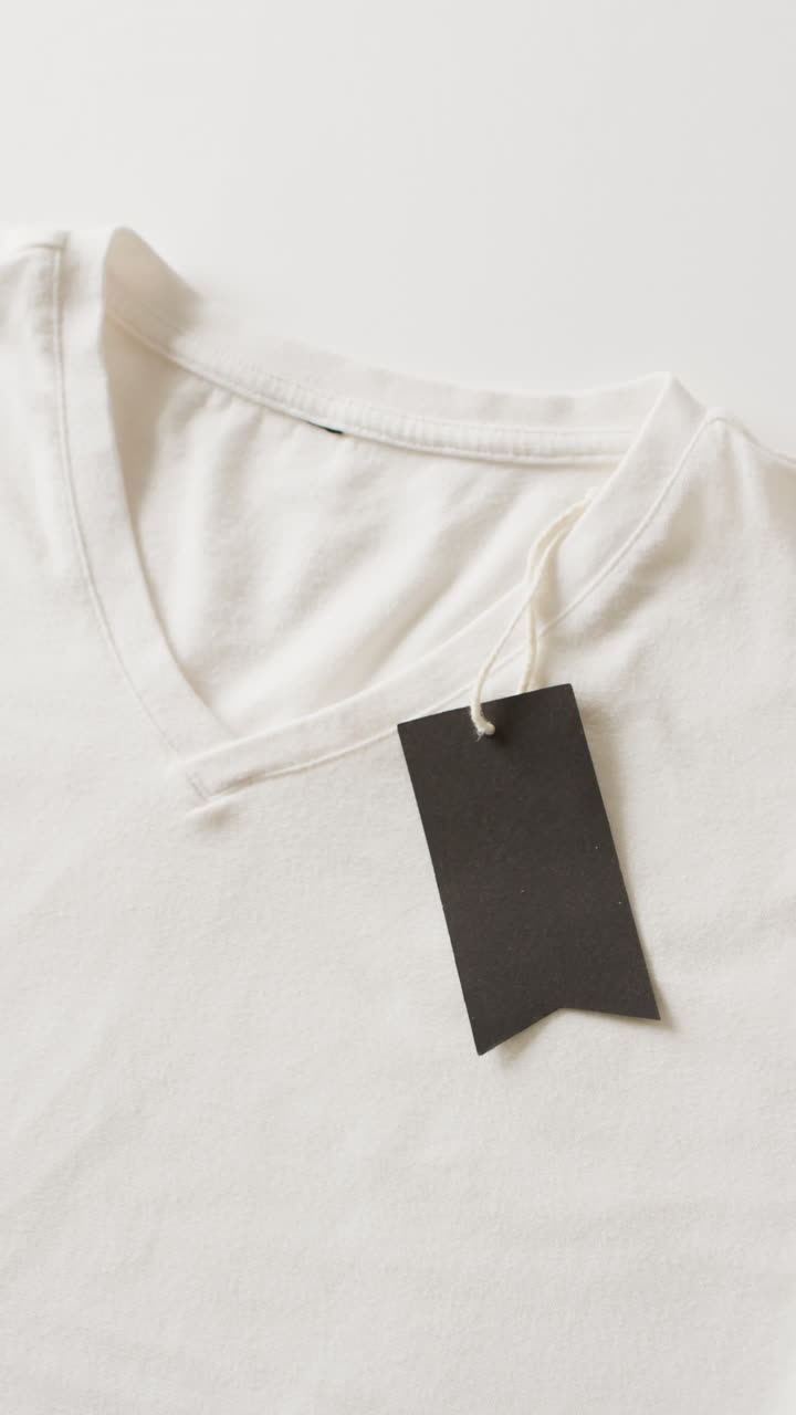 Vertical video of close up of white folded t shirt with tag on white background with copy space