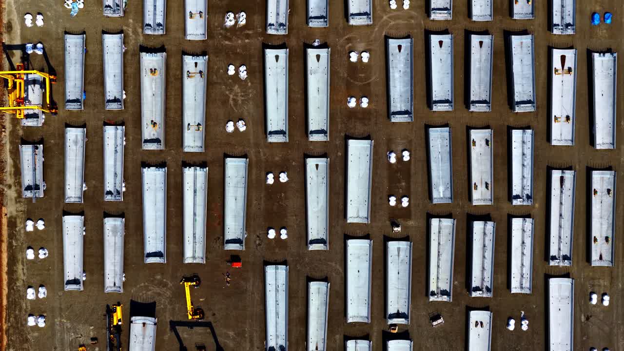 Straight down aerial view of huge wind turbine tower bodies and other parts ready for construction of a wind park or wind farm