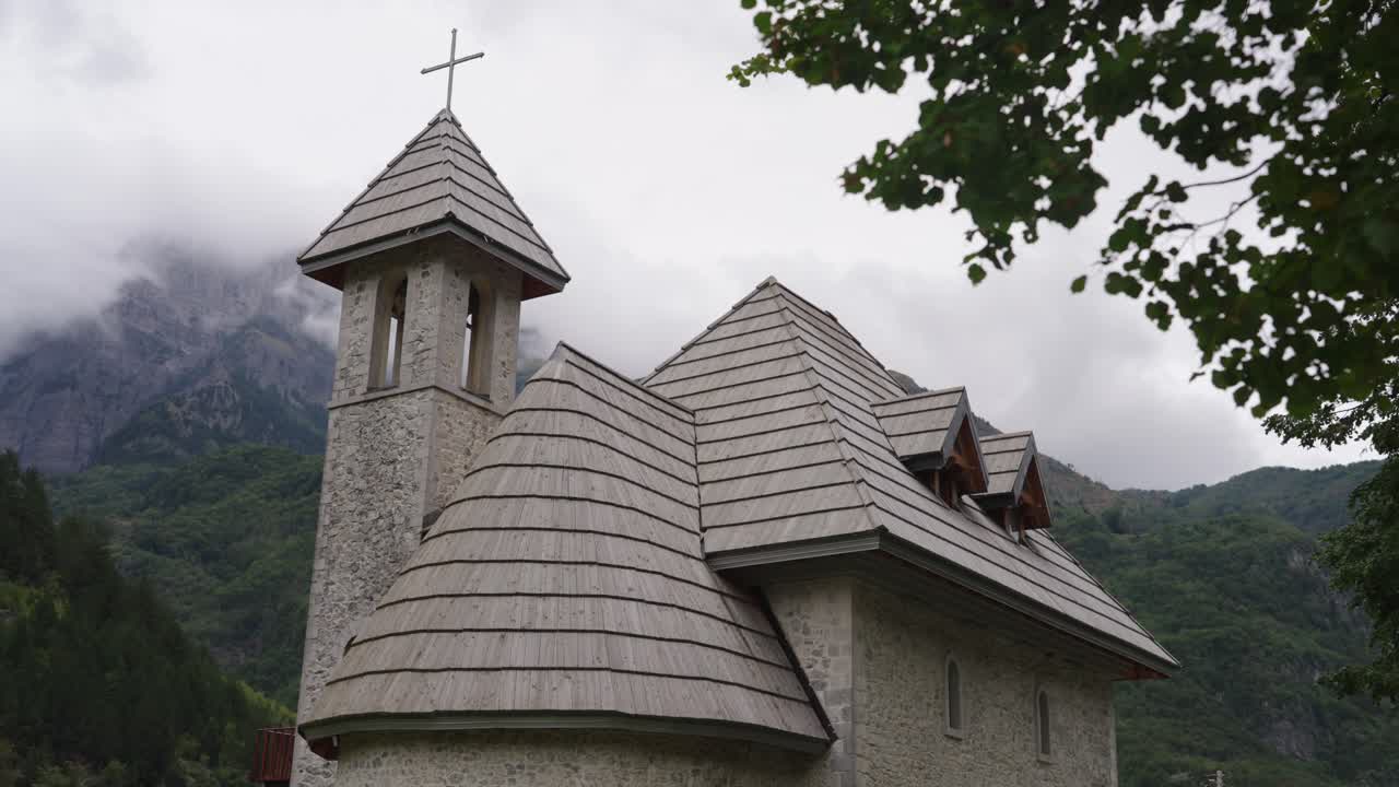 Historic stone church with a shingle roof in a mountain valley on a gloomy day