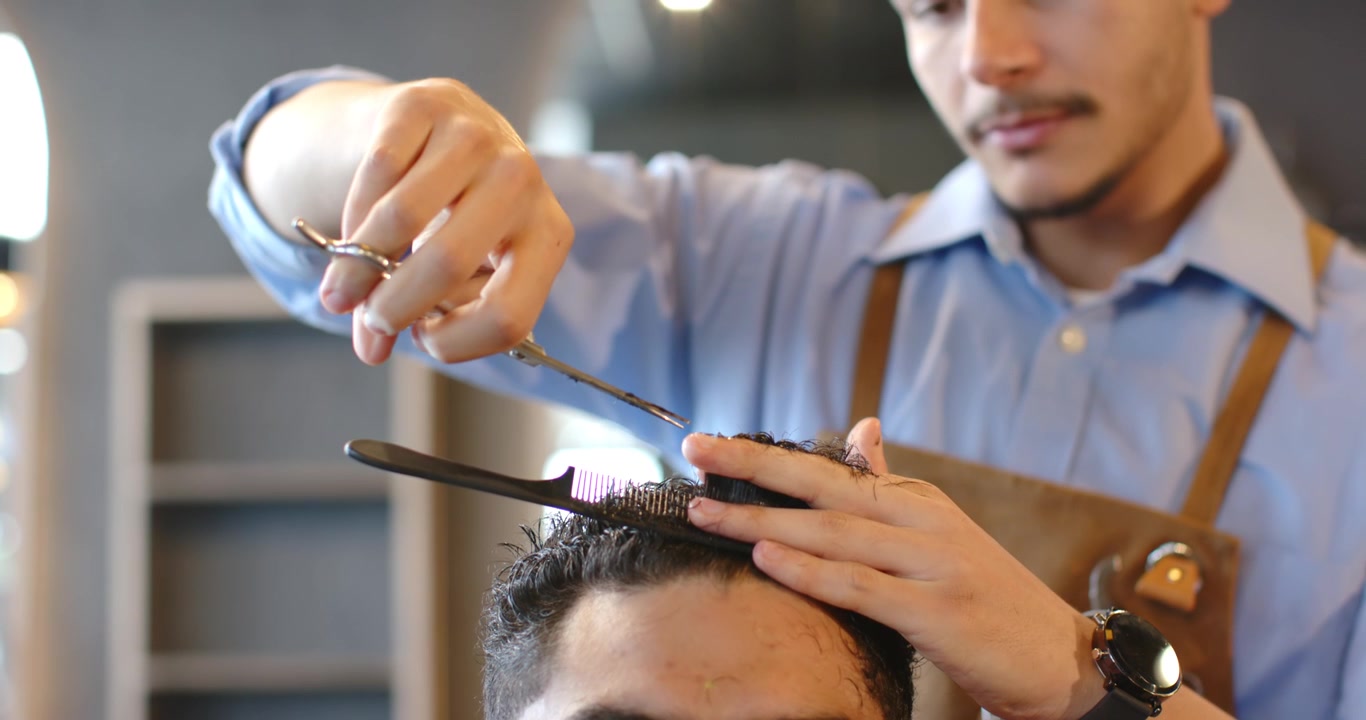 Uomo afroamericano seduto sulla poltrona del barbiere, il barbiere gli pettina e taglia i capelli in cima con le forbici