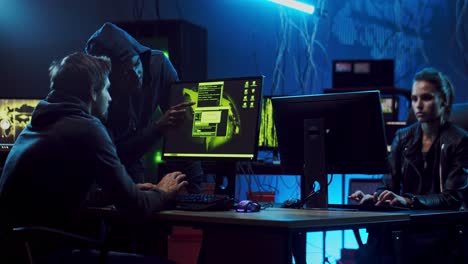 two male and female software developers or hackers working at computers in the dark room, man helping to hack programs and giving advice